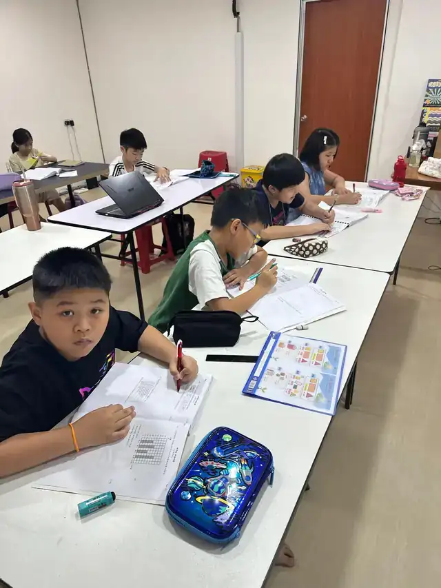孩子在课室里做练习本，桌上放着中心的文件夹